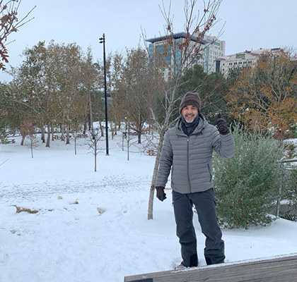 Abel wearing jacket and beanie standing in a park on a snowy ground.