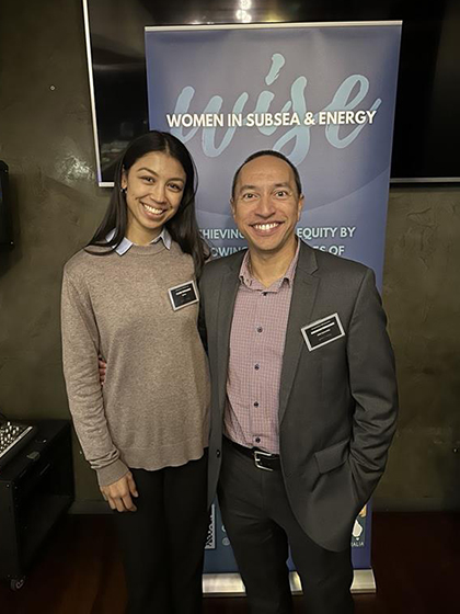 Claire standing next to a work colleague in front of a banner: Women in Subsea & Energy.