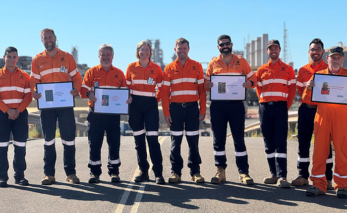 Erica on-site with a group of 8 men wearing PPE and holding awards.