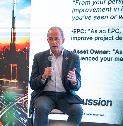 John sitting on a stool on stage speaking into microphone.