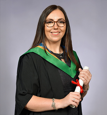 Katie in a graduation gown holding a certificate of her degree.