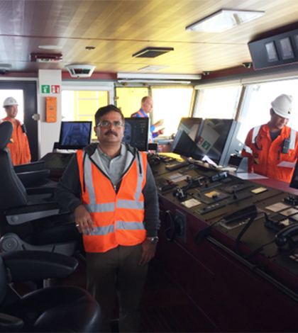 Raj standing in a control room with three other workers.