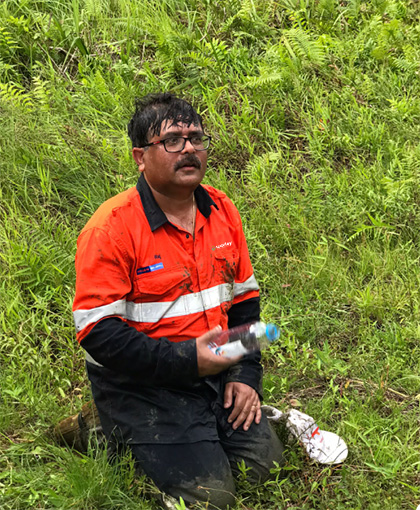 Raj looking sweaty while kneeling on grass holding a bottle of water.