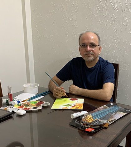 Shripad sitting at a desk with paints and brushes, in front of his painting.