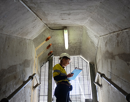 Sonel inside dam walls wearing PPE and holding a clipboard.