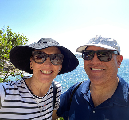 Vicki standing next to her partner outside on a cliff overlooking the ocean.