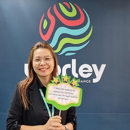Weerapa holding a sign that says "I dedicate myself to enhancing customer satisfaction through quality initiatives.