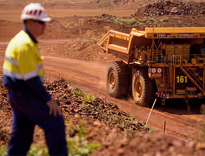 Nick wearing hard hat on a mining site with mine truck nearby.