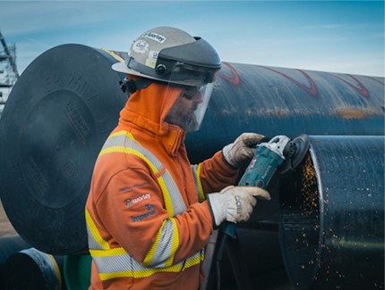 Worley construction worker wearing PPE using a tool on a large steel pipe.