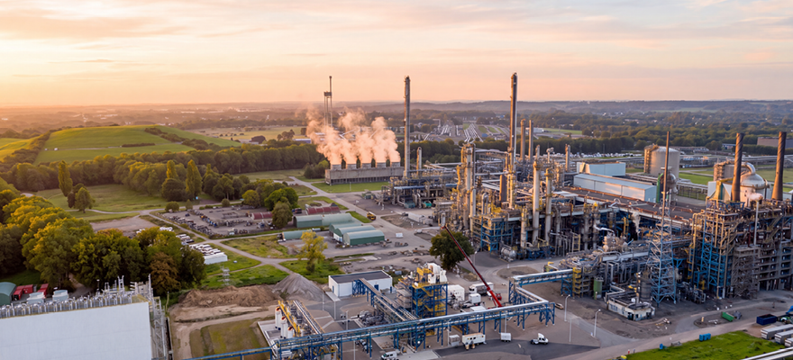 Large chemical processing plant with distillation towers, process units and surrounding industrial infrastructure at sunset.