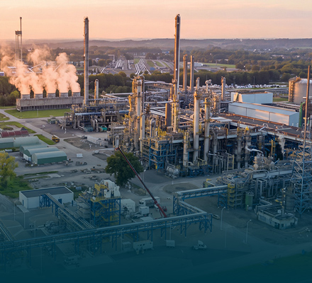 Large chemical processing plant with distillation towers, process units and surrounding industrial infrastructure at sunset.