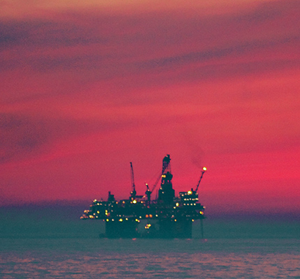 Offshore oil rig in the ocean with a red sky.