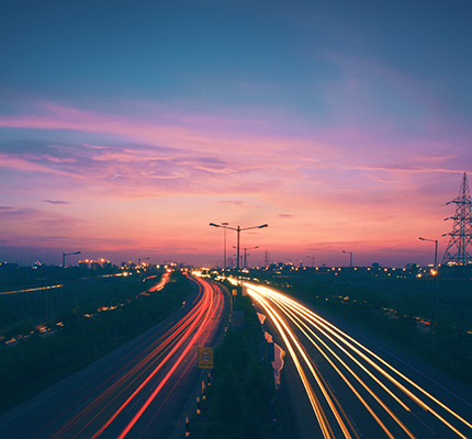 Highway at sunset with power lines and vehicle light trails.