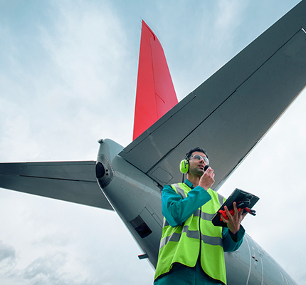 Aeronautical engineer in front of an airplane wearing ear protection talking into a handheld device.