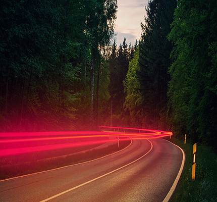 Vehicle red tail lights along a winding road through a forest.