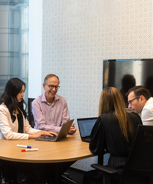 Four people sitting together at a desk working together on their laptops.