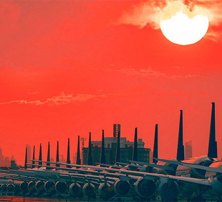 Rows of aircraft parked at an airport runway at sunset.