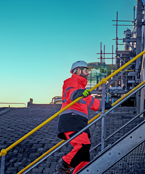 Person wearing PPE walking up stairs in a steel structure.