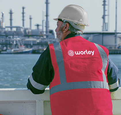 Man wearing PPE looking over the water to a refinery.