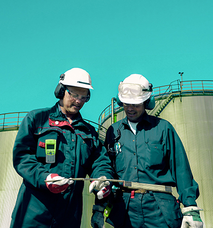 Two people wearing green personal protective equipment at a work site.