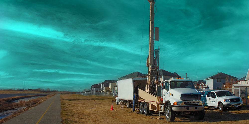 Truck with machinery parked next to a road and houses.