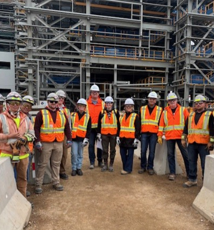 Cheryl standing with several colleagues wearing safety equipment in front of a large construction on site.