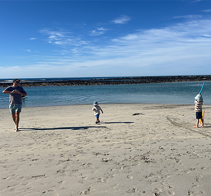 Craig with two little children playing cricket on the beach.