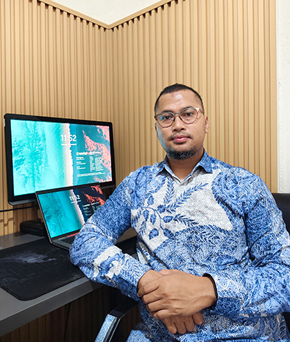 Febry sitting in front of computer screens in the office.