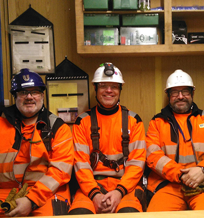 Gavin sitting with two colleagues inside a site office, wearing PPE.