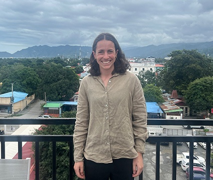 Hannah standing on a balcony overlooking a town with low-set buildings and mountains.