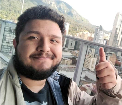 Juan with his thumbs up gesture with city buildings in the background.