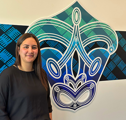 Kaitlin standing next to a piece of Indigenous artwork on the wall.