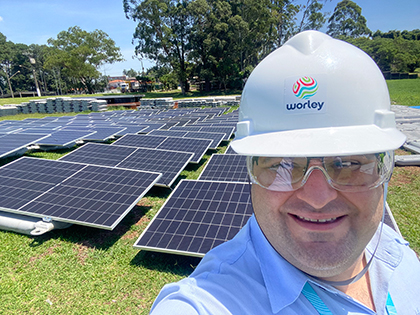 Leandro wearing a hardhat and goggles in front of rows of solar panels on the ground.