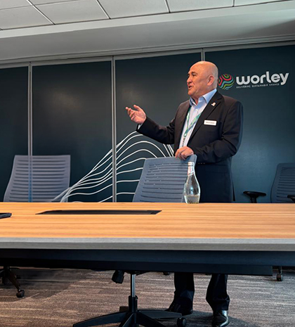 Manuel standing behind a desk presenting to colleagues in a meeting room.