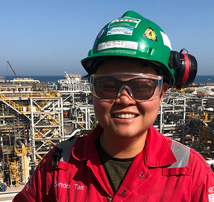 Sandra wearing a safety gear standing on an offshore industrial facility with processing structures visible in the background.