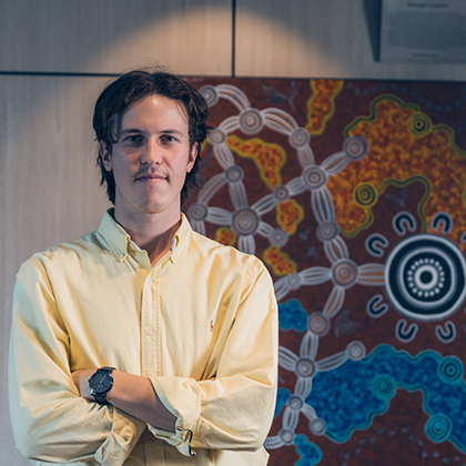 Denzel standing in front of Indigenous artwork in a Worley office.