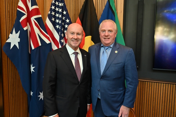 Greg Moriarty and Chris Ashton posing in front of a group of flags.