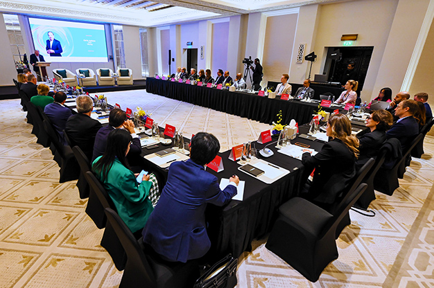 U-shaped table with large group of people at COP28 listening to a speaker at the front.