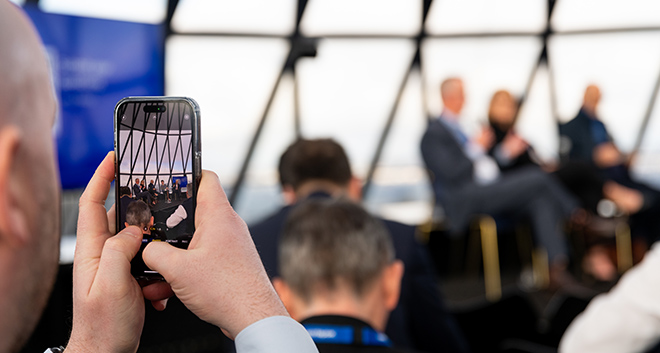 Person looking through their mobile phone to take a photo of the panel at the UK Breakfast Briefing.