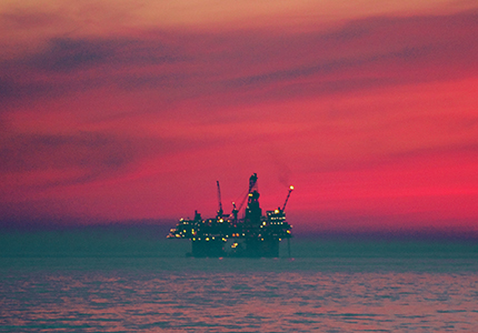 Offshore oil rig in the ocean with a red sky.