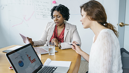 Two women sitting together at a desk looking at a laptop.