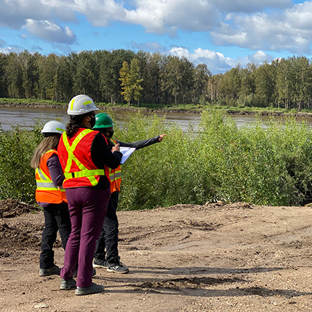 Three people wearing PPE standing together looking at a body of water.