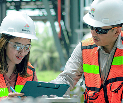 Man and woman wearing hard hat outdoors looking at a clipboard.